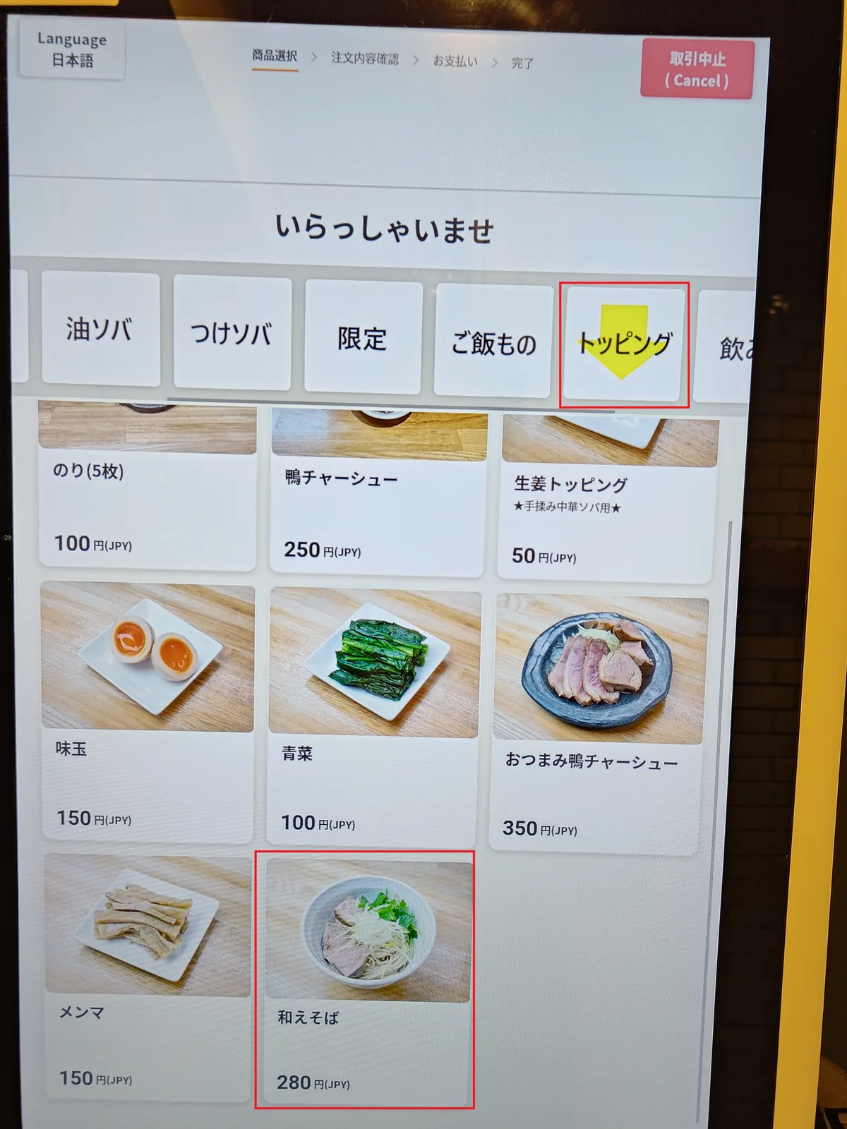 Der Topping-Bildschirm des Ticketautomaten. Der 'トッピング' (Toppings) Tab oben ist rot umrandet, und '和えそば ¥280' (Aezoba ¥280) unten ist ebenfalls rot umrandet. Auf demselben Bildschirm sind auch Nori (5 Blatt) ¥100, Enten-Chashu ¥250, Ingwer-Topping ¥50, Ajitama ¥150, Grünzeug ¥100, Otumami Enten-Chashu ¥350, Menma ¥150 aufgeführt. How to find aezoba topping on a Japanese ramen vending machine.