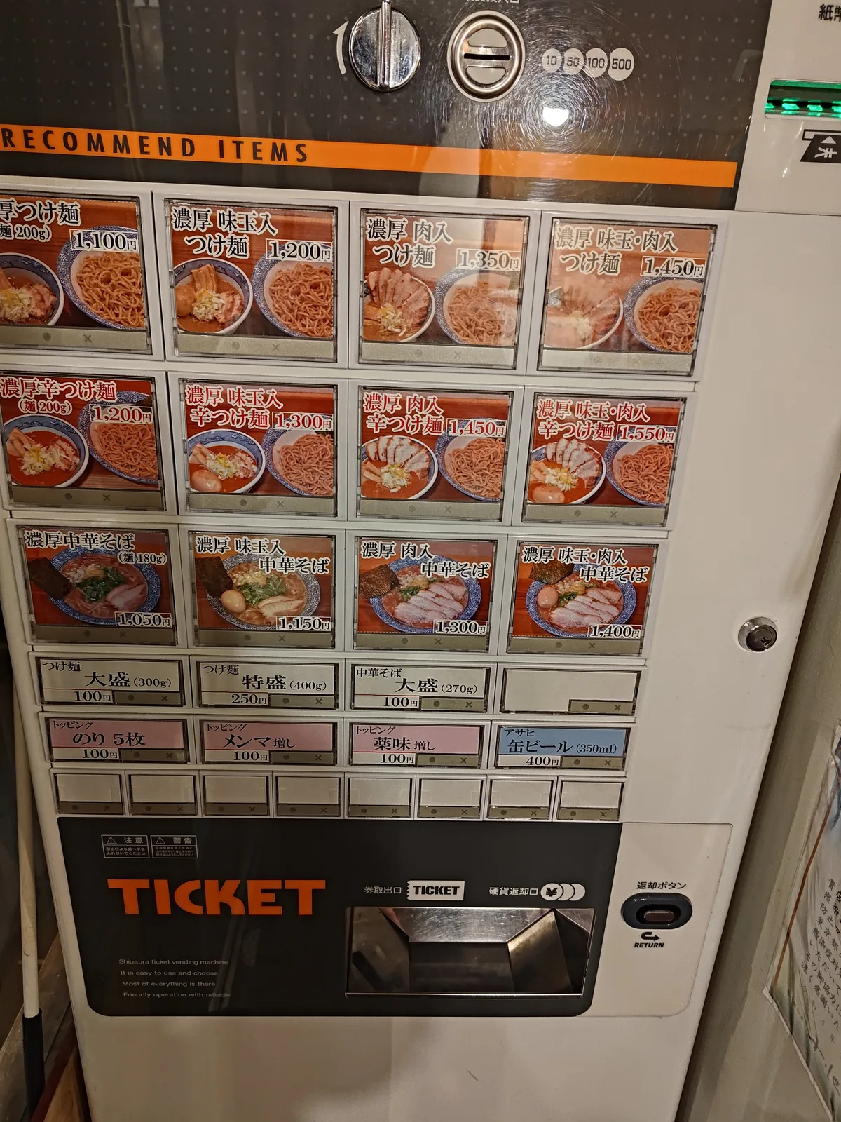 Japanese ramen shop ticket machine at Dogenzaka Manmosu in Shibuya, Japan. Photos clearly show tsukemen, spicy tsukemen, and chuka soba. Options for large portions and toppings are also visible. Ideal for tourists seeking ramen in Japan.