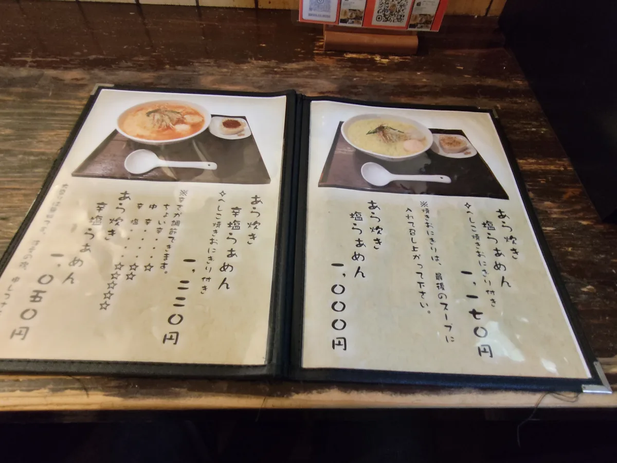 日文菜單本打開的樣子。附有Ara-daki Shio Ramen和Koshio Ramen的照片頁。日本拉麵、菜單、麵屋海神、點餐