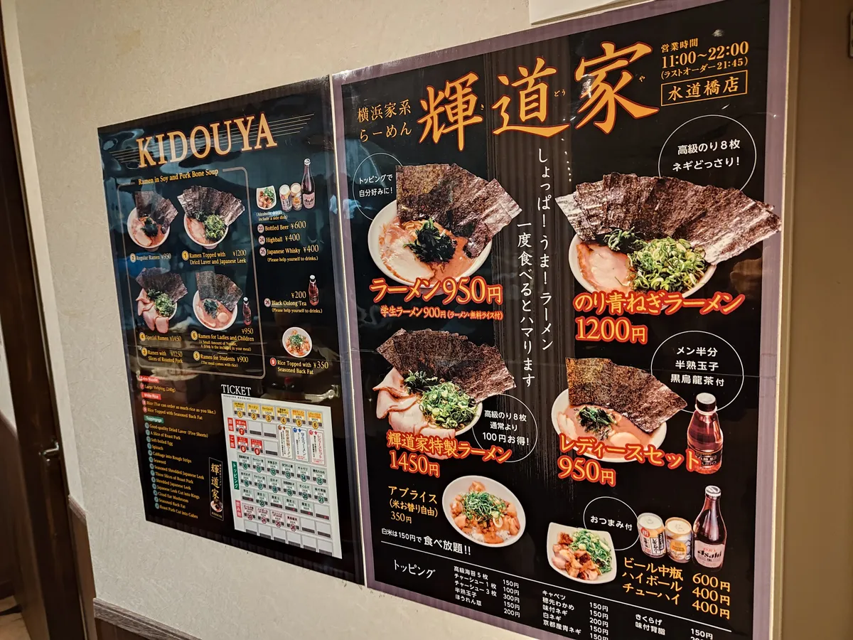店頭のメニュー看板。右側に写真付き日本語メニュー、左側に英語メニューがある。ラーメン¥950、のり背ネギラーメン¥1,200、輝道家特製ラーメン¥1,450などの価格が確認できる。