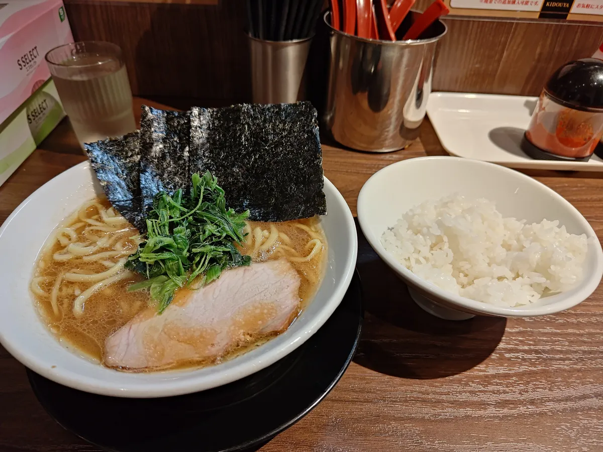 ラーメンとライス。豚骨醤油スープに太めの麺、海苔3枚、ほうれん草、チャーシューが盛り付けられている。横にライスの小鉢。
