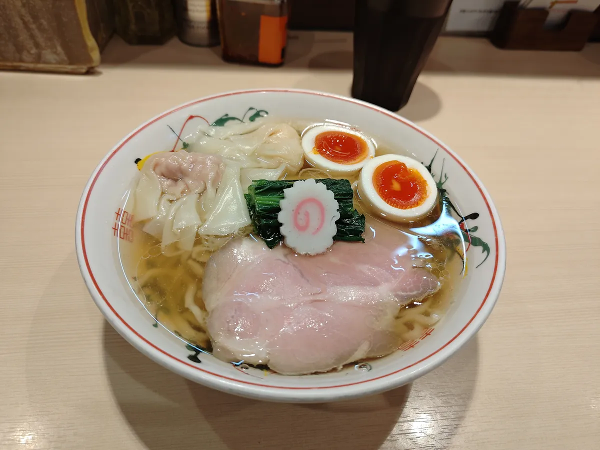 ちょっとずつ白だしラーメン。赤い龍の絵柄が入ったレトロな中華丼に、澄んだ金色の白だしスープ。海老ワンタンと肉ワンタン、半熟味玉、青菜、なると、大判のチャーシューがのり、ちぢれ麺が見える。
