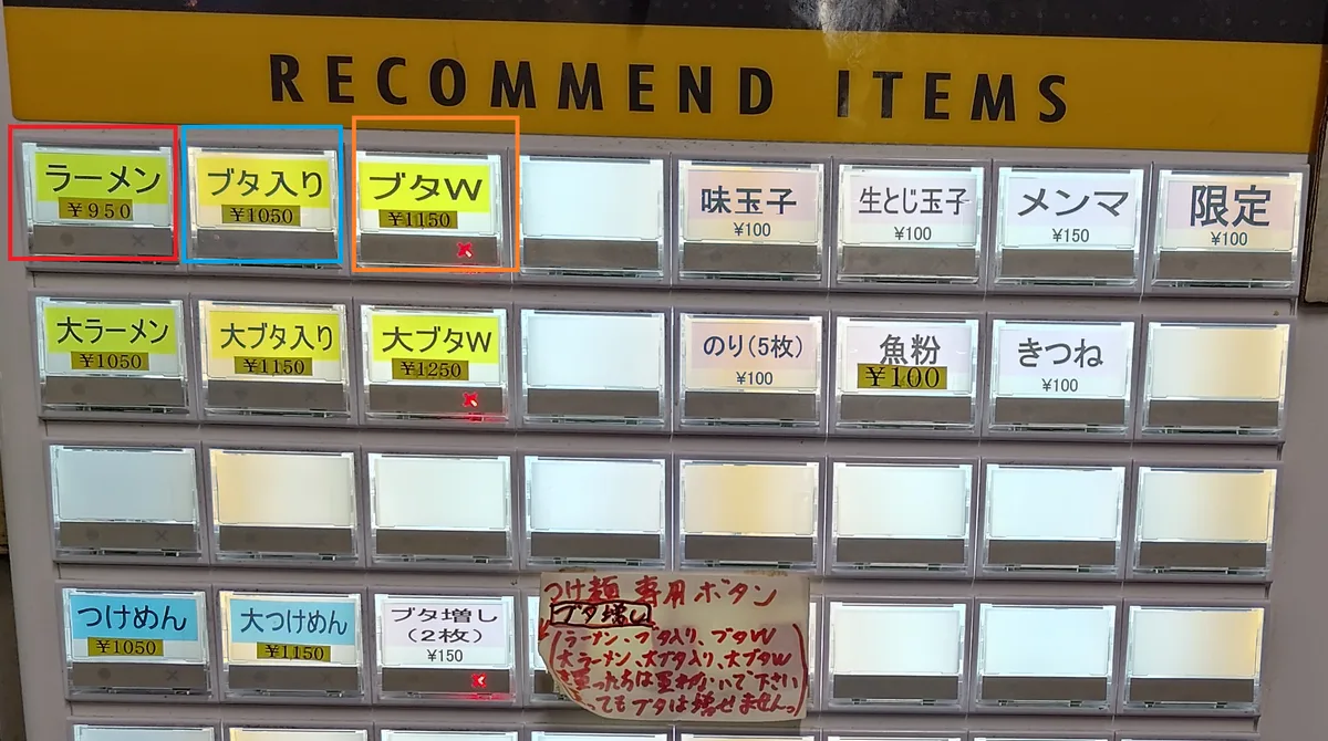 券売機のメニュー詳細。「ラーメン」（赤枠）「ブタ入りラーメン」（青枠）「ブタW」（オレンジ枠）の3つのメインメニューが3色枠で強調され、ほかに大ラーメン・つけ麺・生とじ玉子・魚粉・海苔・メンマなどのトッピングボタンが並ぶ。