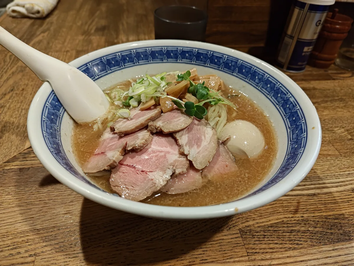 青い縁取りの白い丼に盛られた、燦燦斗のら〜めん＋特増し。スープはほんのり乳白色のかかった魚介豚骨色で、しっとり艶のある厚切り低温調理チャーシュー4〜5枚、半熟味玉、刻みネギとかいわれが彩り、奥には板状メンマが立つ。