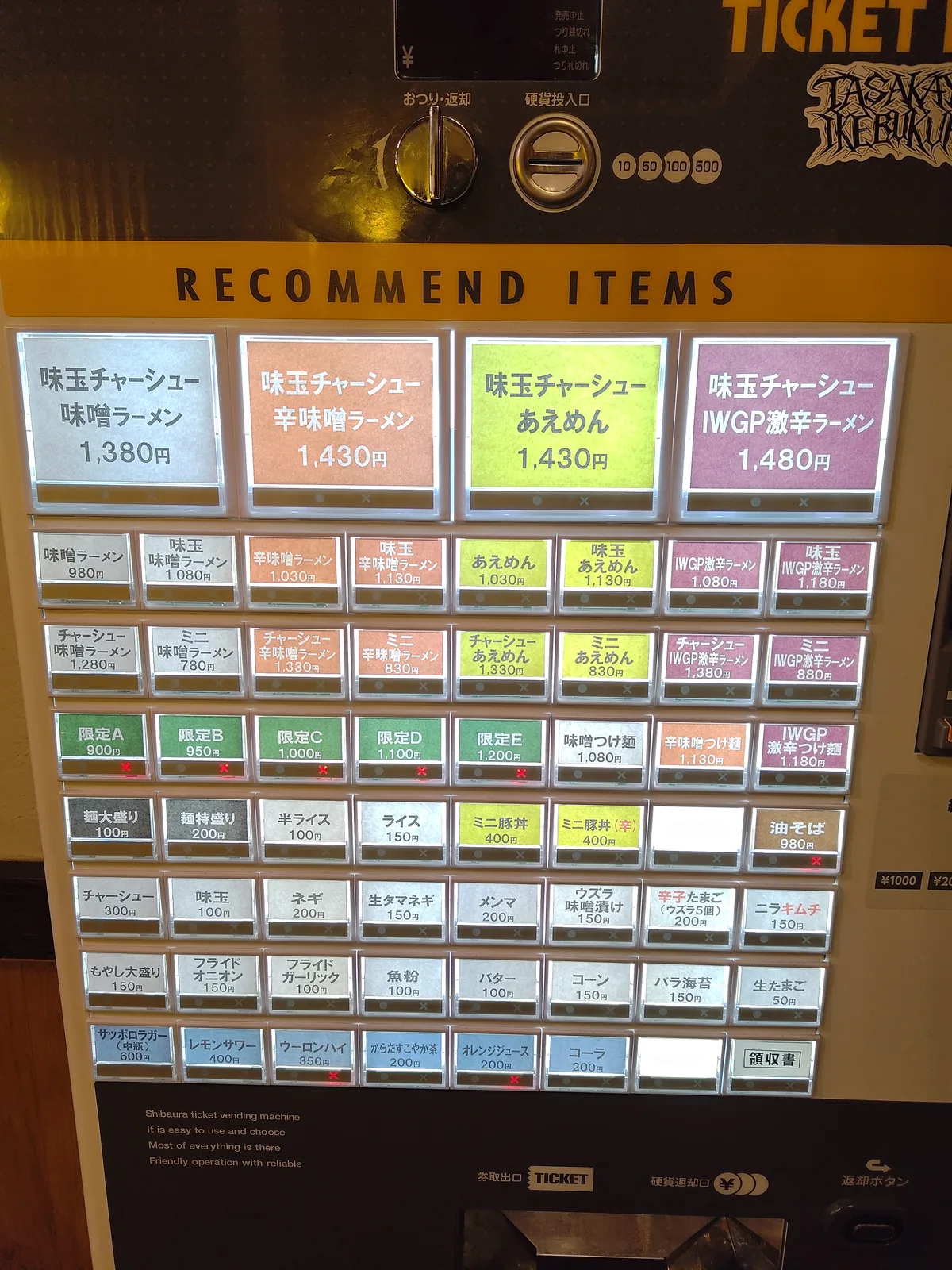 Tasakaya 自動販賣機全貌。上方寫著「RECOMMEND ITEMS」，最上層有四塊大型彩色面板，下方則有大量按鈕呈網格狀排列。全部為日文標示，無照片。 池袋 拉麵 點餐攻略 Miso Ramen